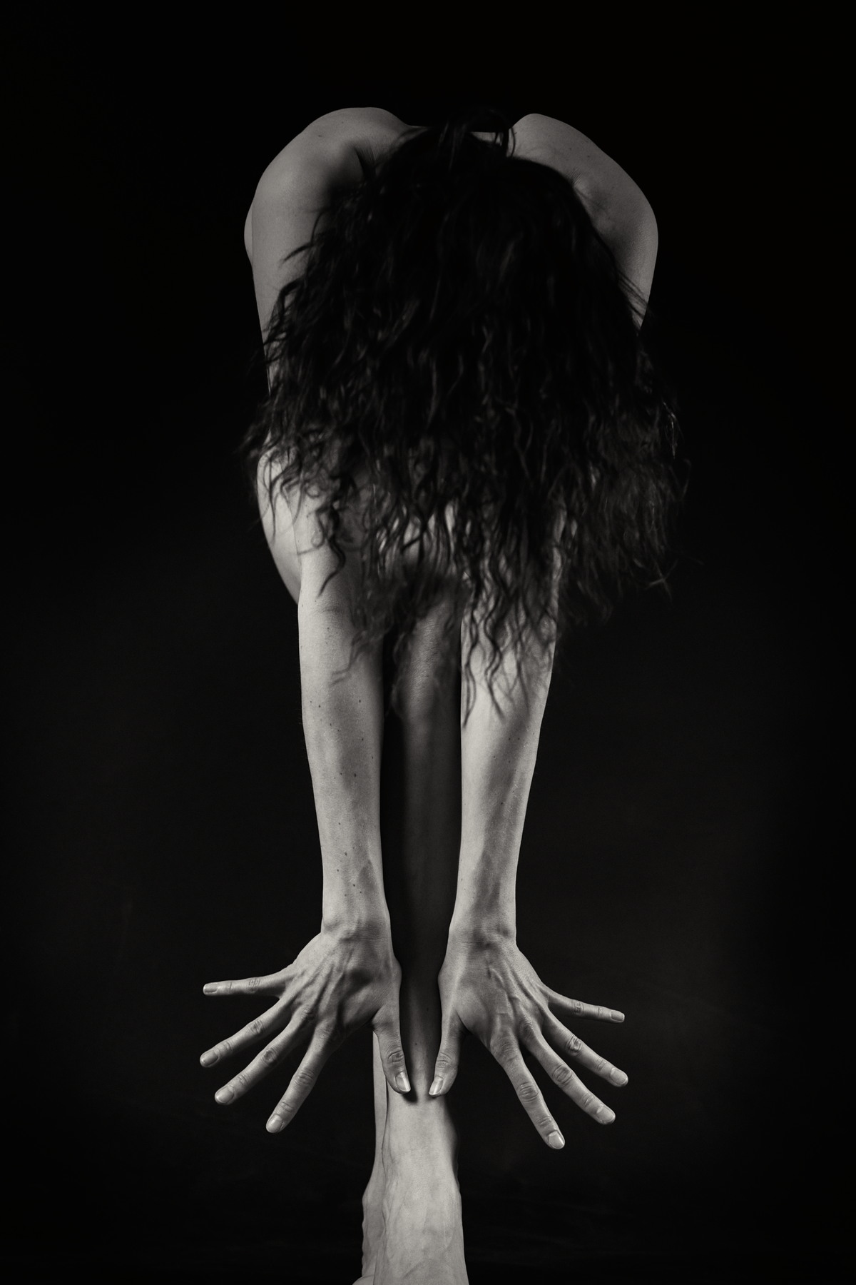 Figure folded forward with both arms extended toward the floor.