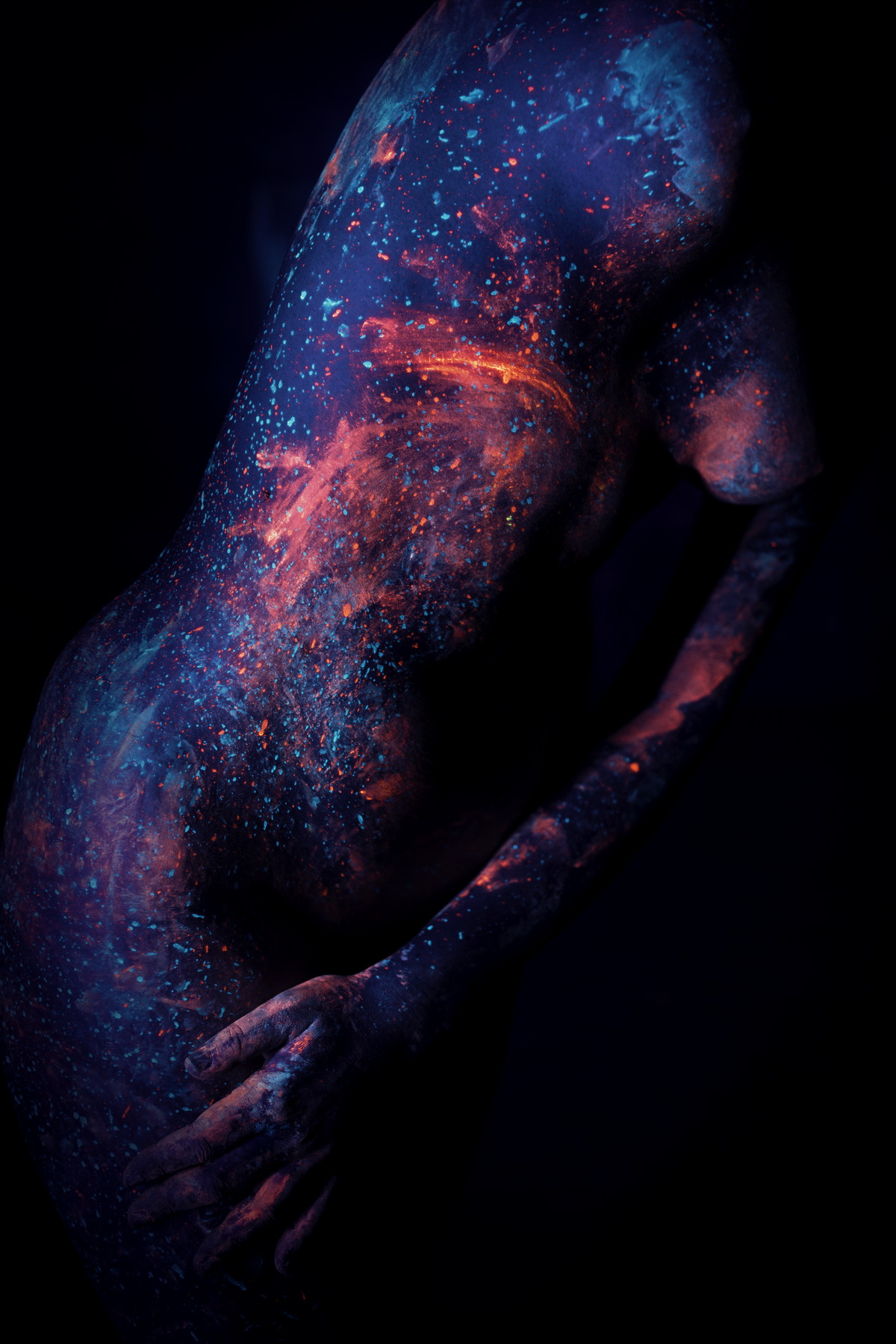 Close view of a torso and hands lit by ultraviolet light.