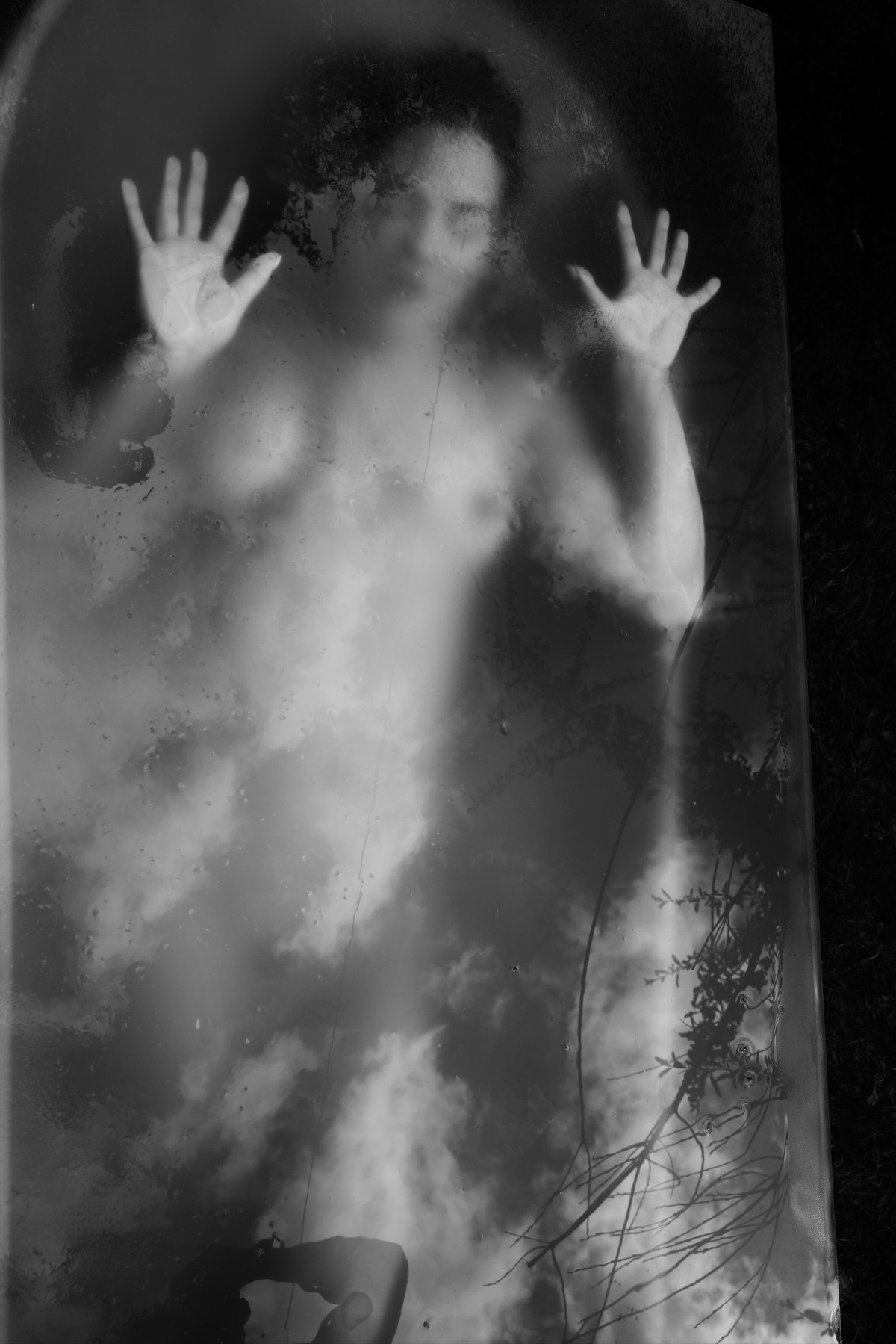 Semi-blurred nude figure pressing both hands against translucent glass.