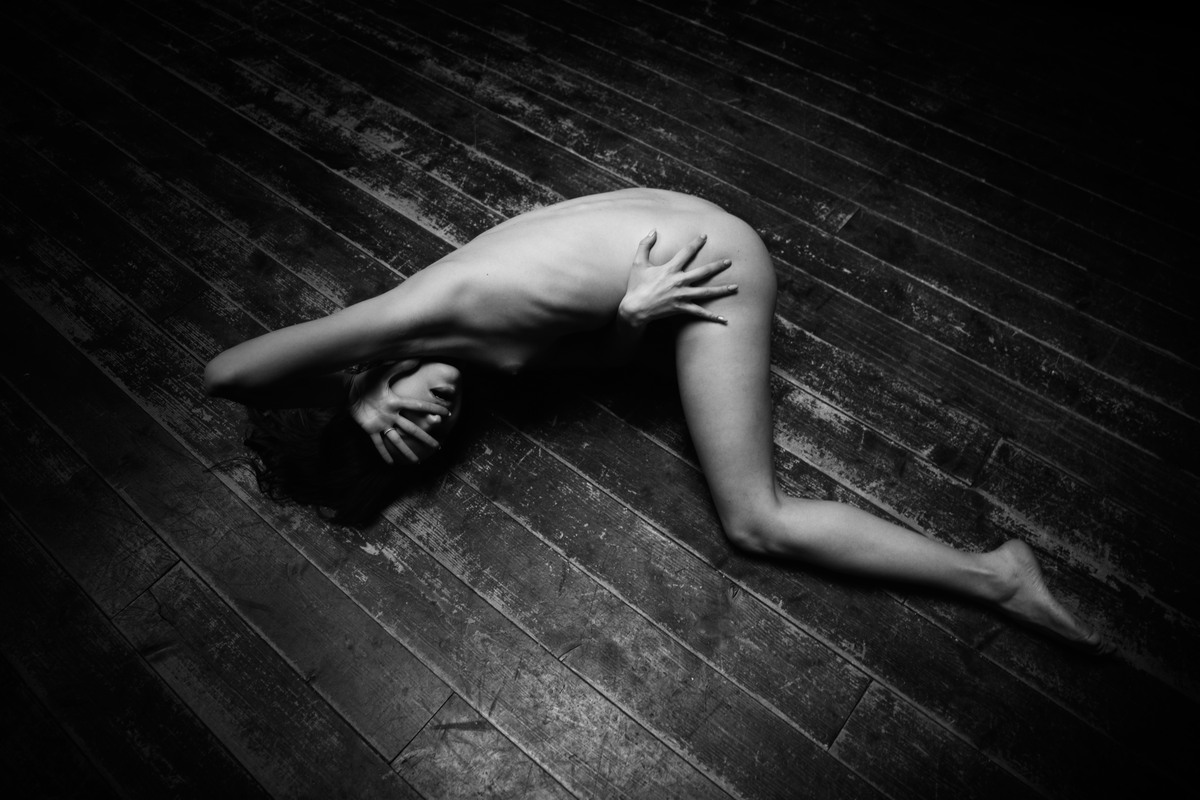 Nude figure arched on a wooden floor in black and white.
