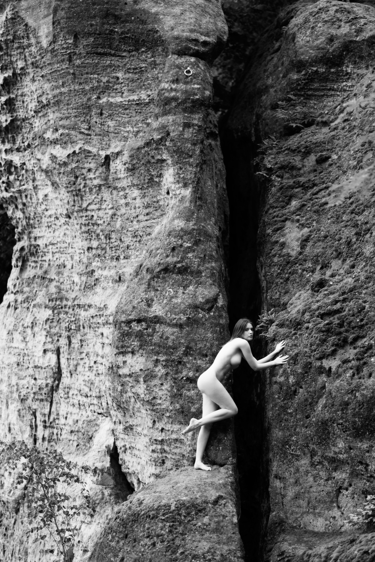 Nude figure climbing within a narrow cleft in a rock face.