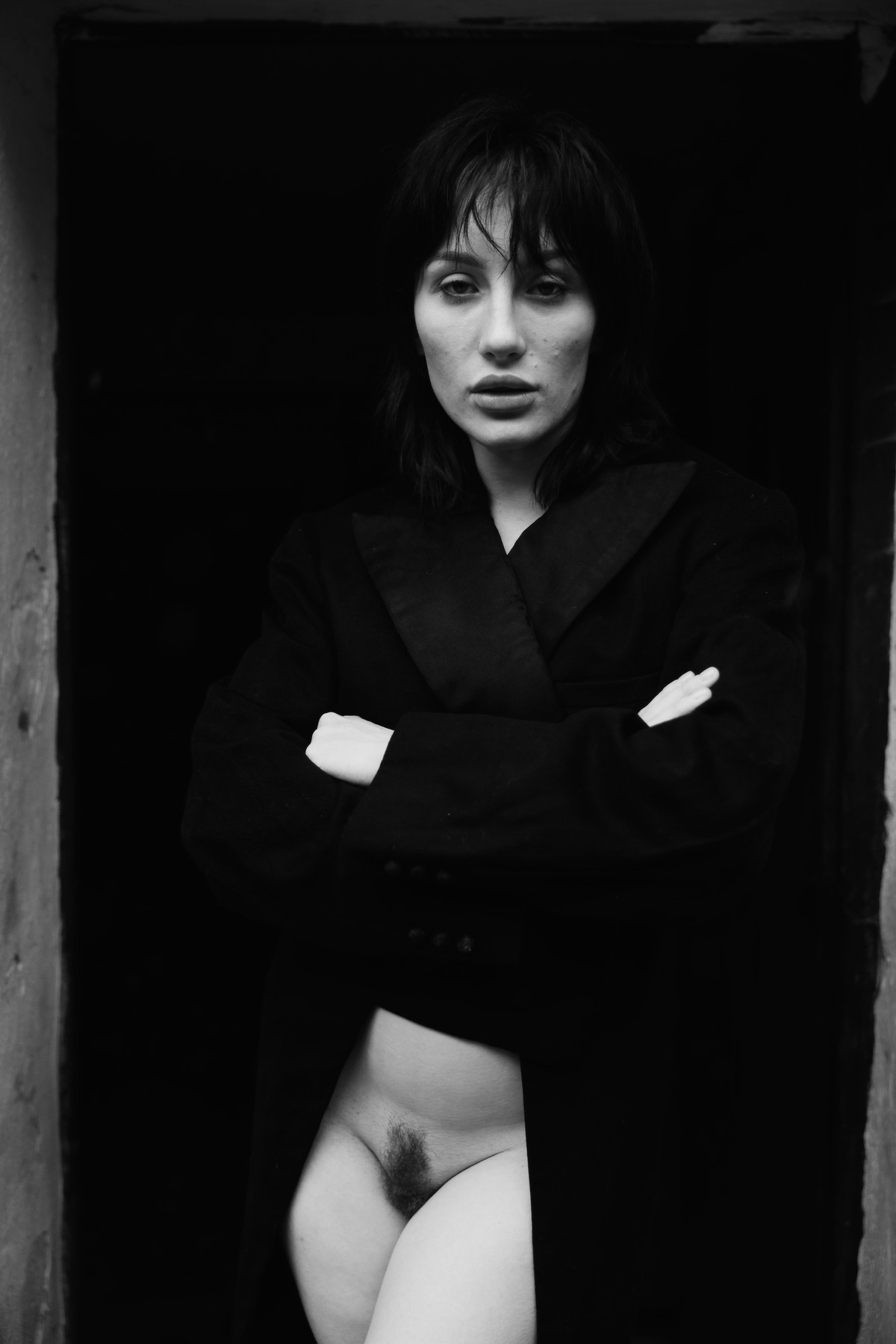 Woman standing in a doorway, bare from the waist down, with arms folded.