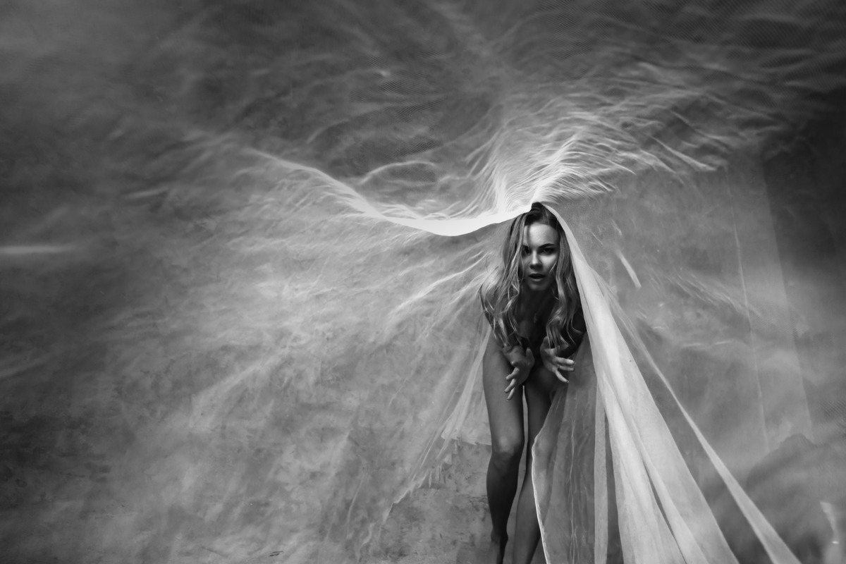 Figure wrapped in flowing translucent fabric against a smoky textured background.