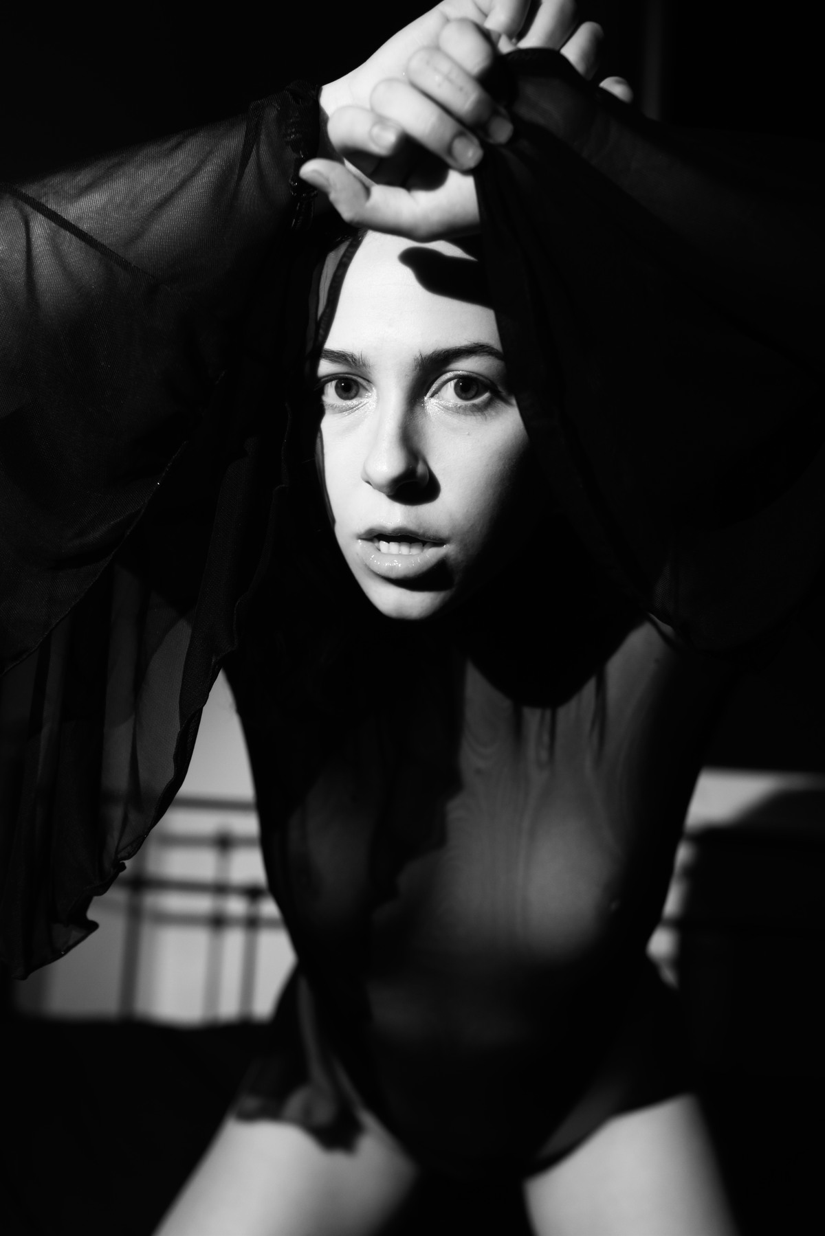 Close portrait of a woman crouching with one arm raised over her head.