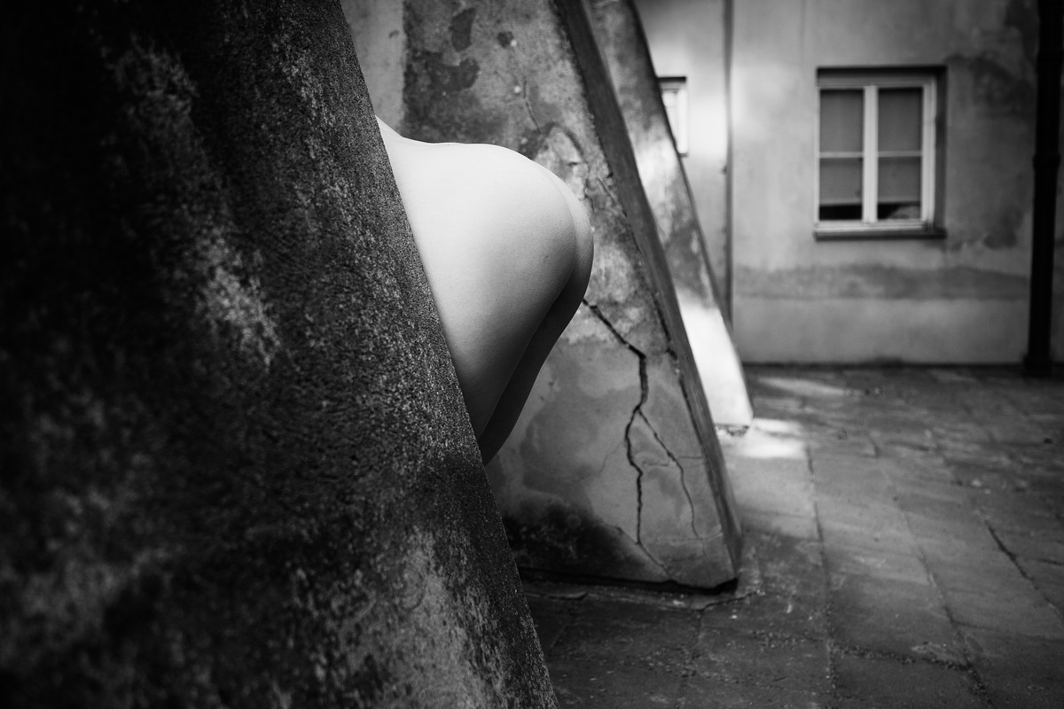 Close crop of a nude figure partly visible between structural elements.