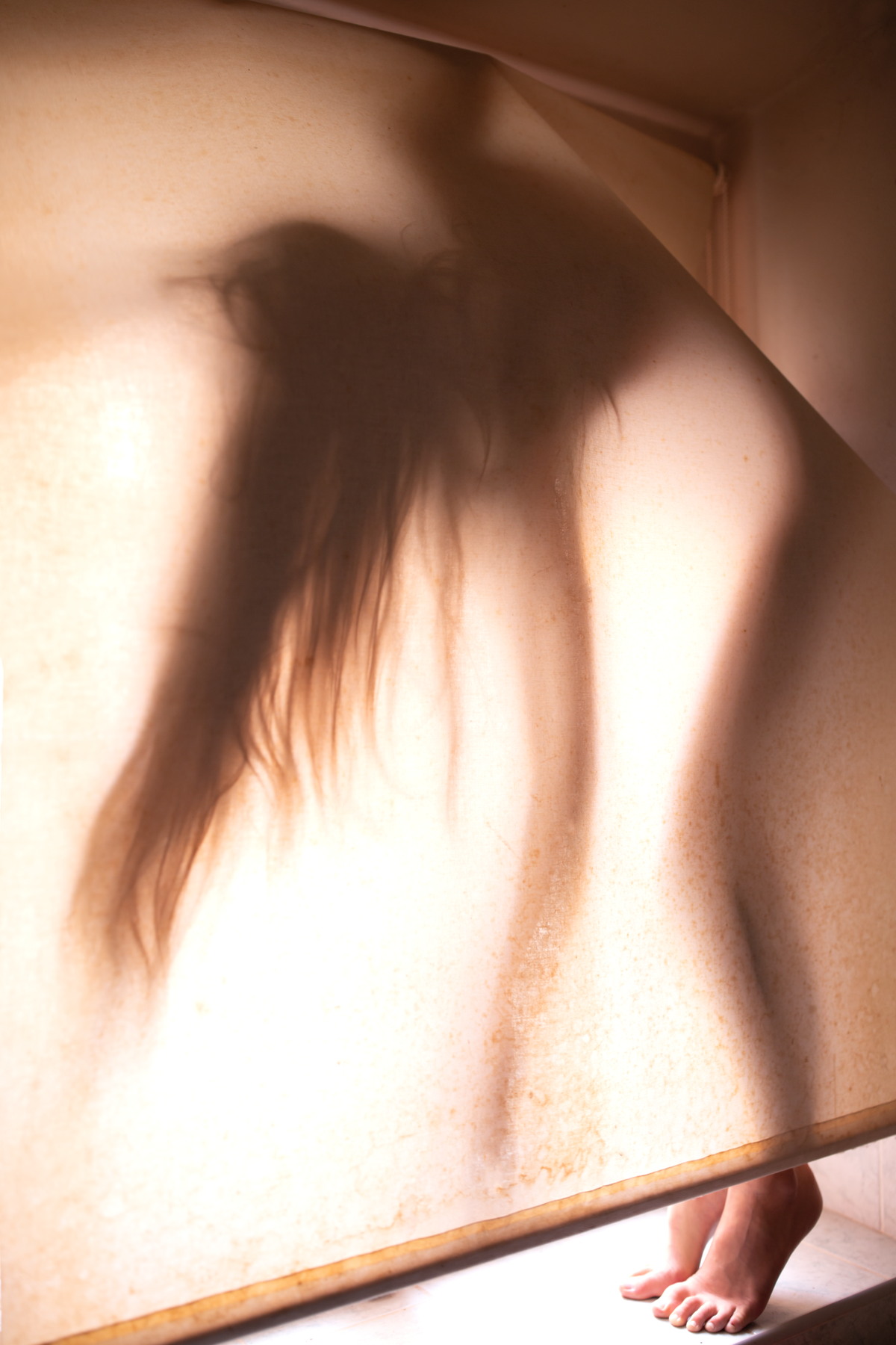 Blurred silhouette of a figure behind warm translucent fabric, with feet slightly visible.