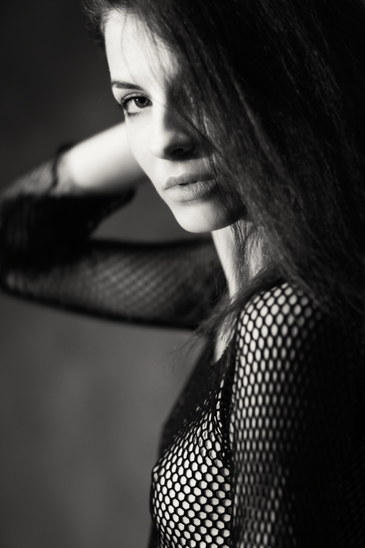 Black-and-white close portrait of a woman in a mesh top, partly obscured by her hair.
