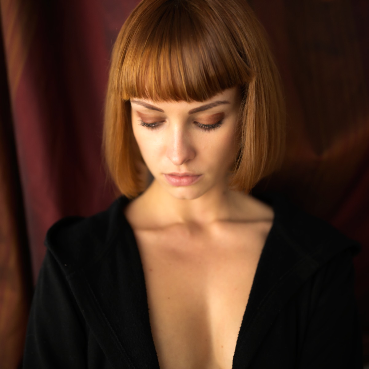 Color portrait of a woman with a short red bob looking downward.