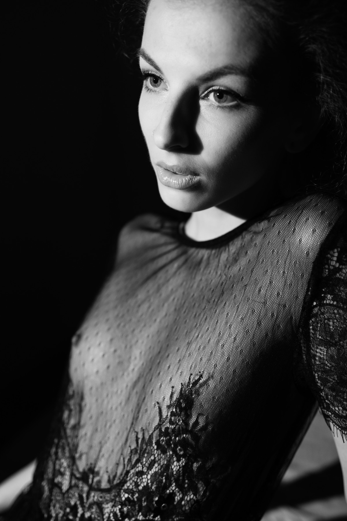 Low-key black-and-white portrait of a woman in a lace top lit from the side.