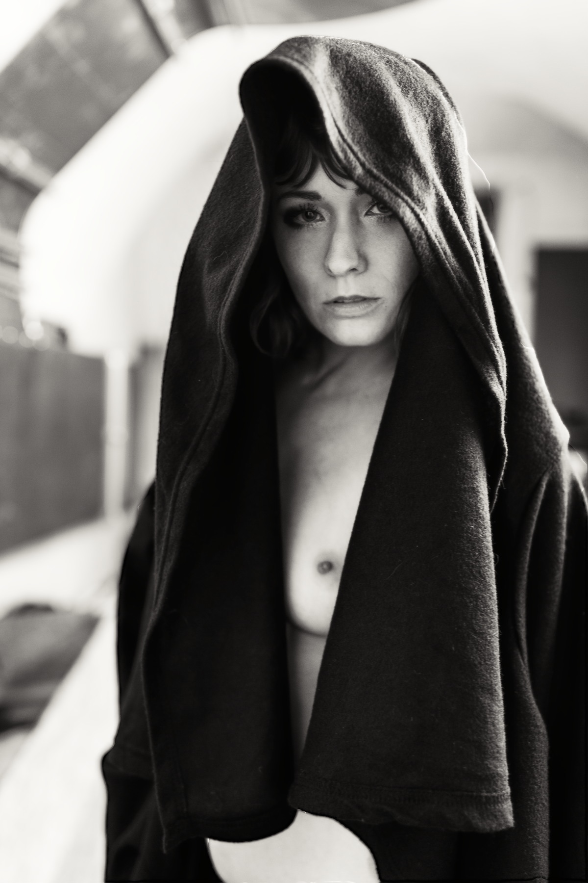Black-and-white portrait of a nude woman partly wrapped in a dark blanket.