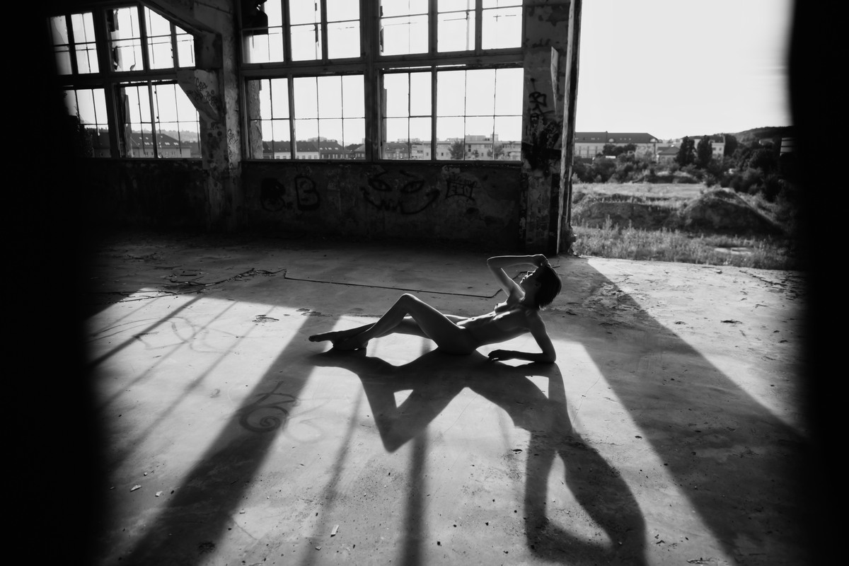 Figure lying in an abandoned hall, casting long angular shadows.