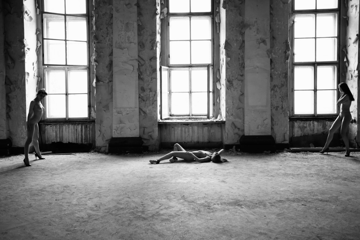 Three figures spaced across a derelict room with tall windows.