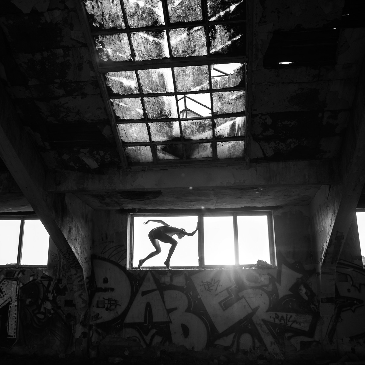 Silhouetted figure leaping across a window opening in a ruined building.