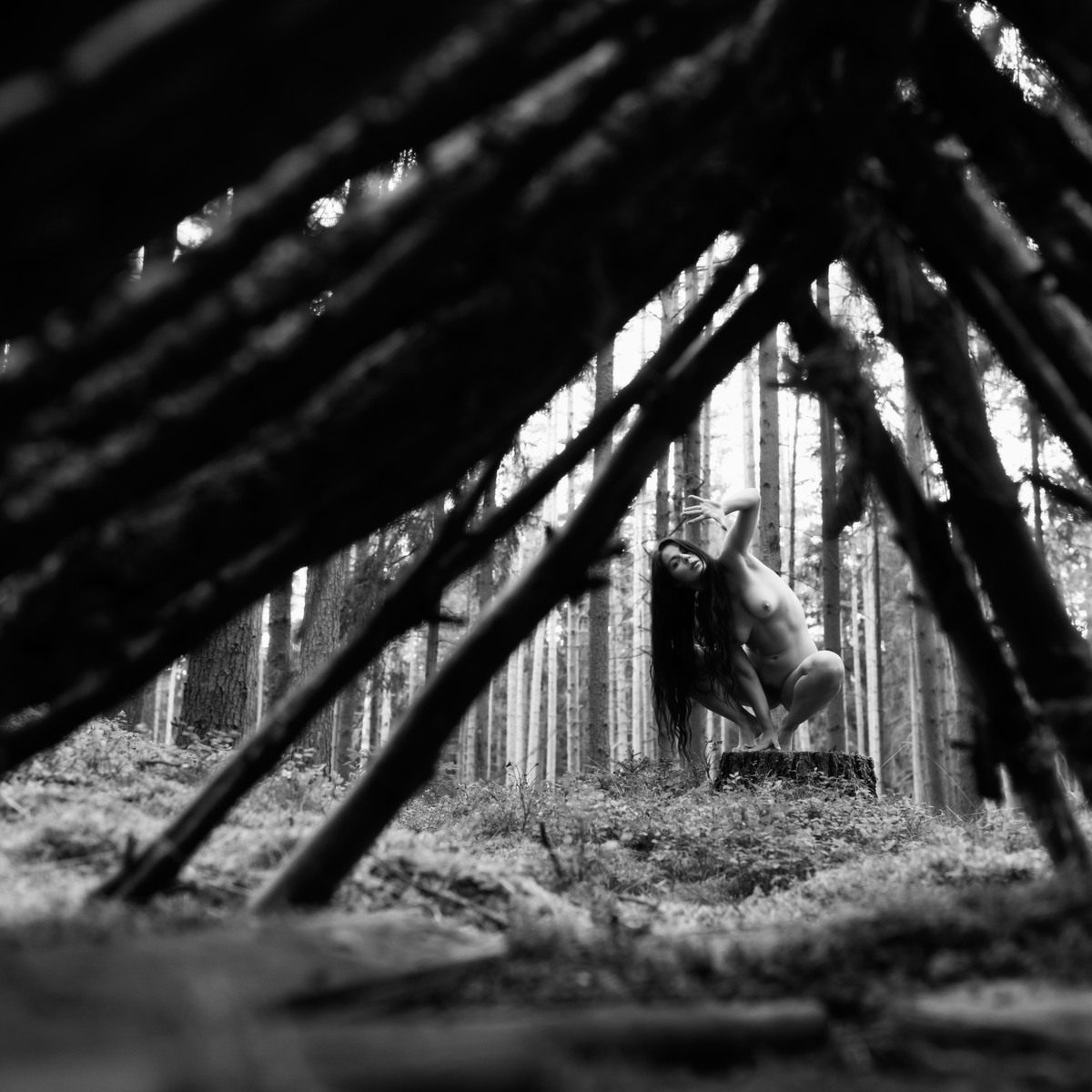 Figure crouched inside a triangular structure of wooden poles.